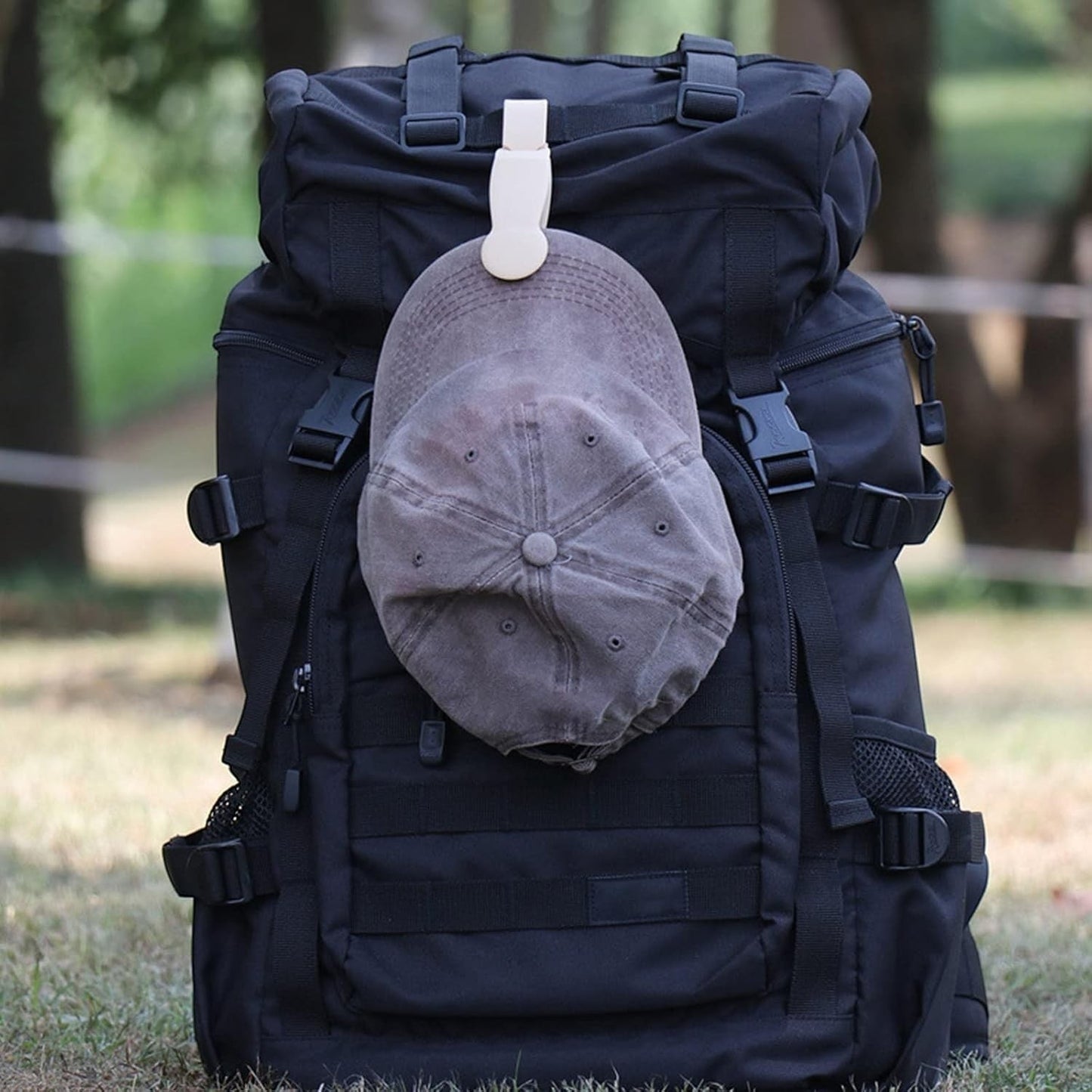 Waf Store Lebanon beige silicone hat clip attached to a black backpack holding a grey baseball cap outdoors