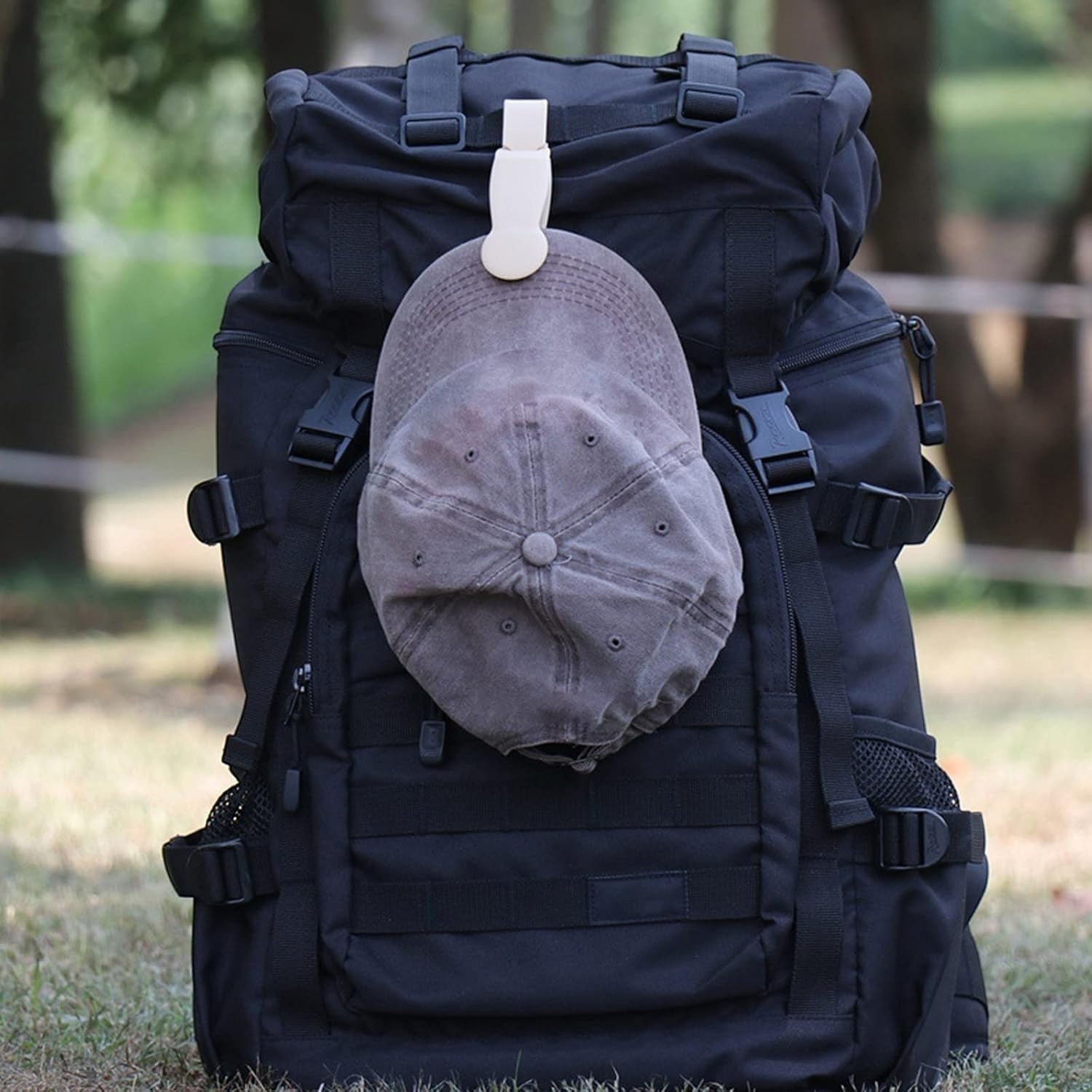 Waf Store Lebanon beige silicone hat clip attached to a black backpack holding a grey baseball cap outdoors